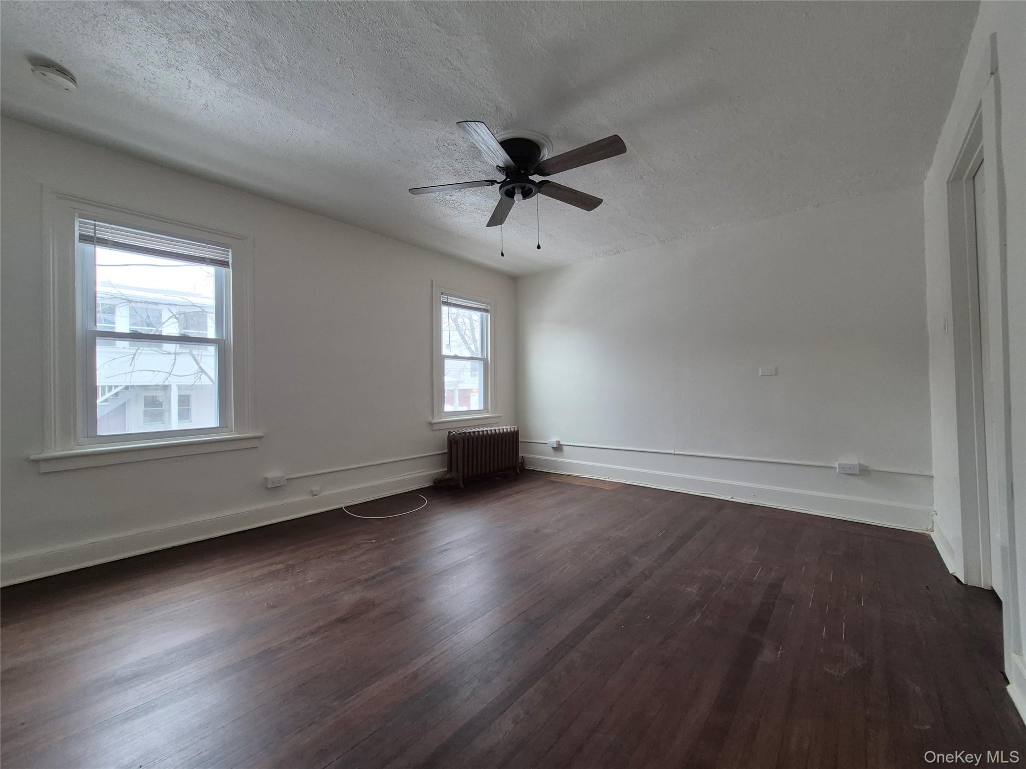 207 Mill Street Poughkeepsie, NY 12601 - Photo 5 of 6 Unfurnished room with radiator, dark wood-type flooring, ceiling fan, and a textured ceiling
