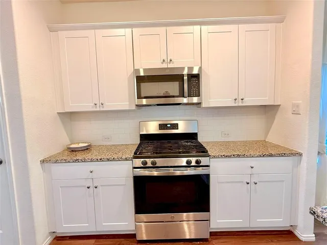 a kitchen with stainless steel appliances granite countertop white cabinets and a stove a oven with wooden floor