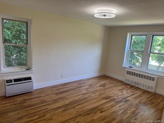 250 West Merrick Road, Unit 2R Freeport, NY 11520 - Photo 14 of 25 Empty room featuring wood finished floors, radiator heating unit, and a wall unit AC