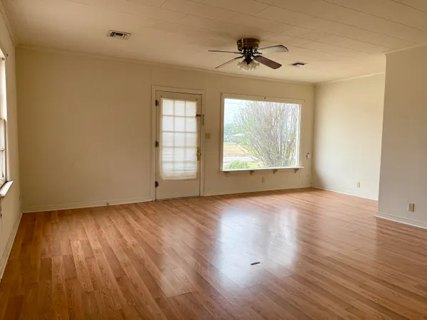 an empty room with wooden floor chandelier fan and windows
