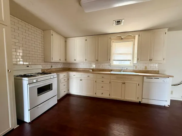 a kitchen with stainless steel appliances granite countertop white cabinets a sink a stove a microwave and wooden floors