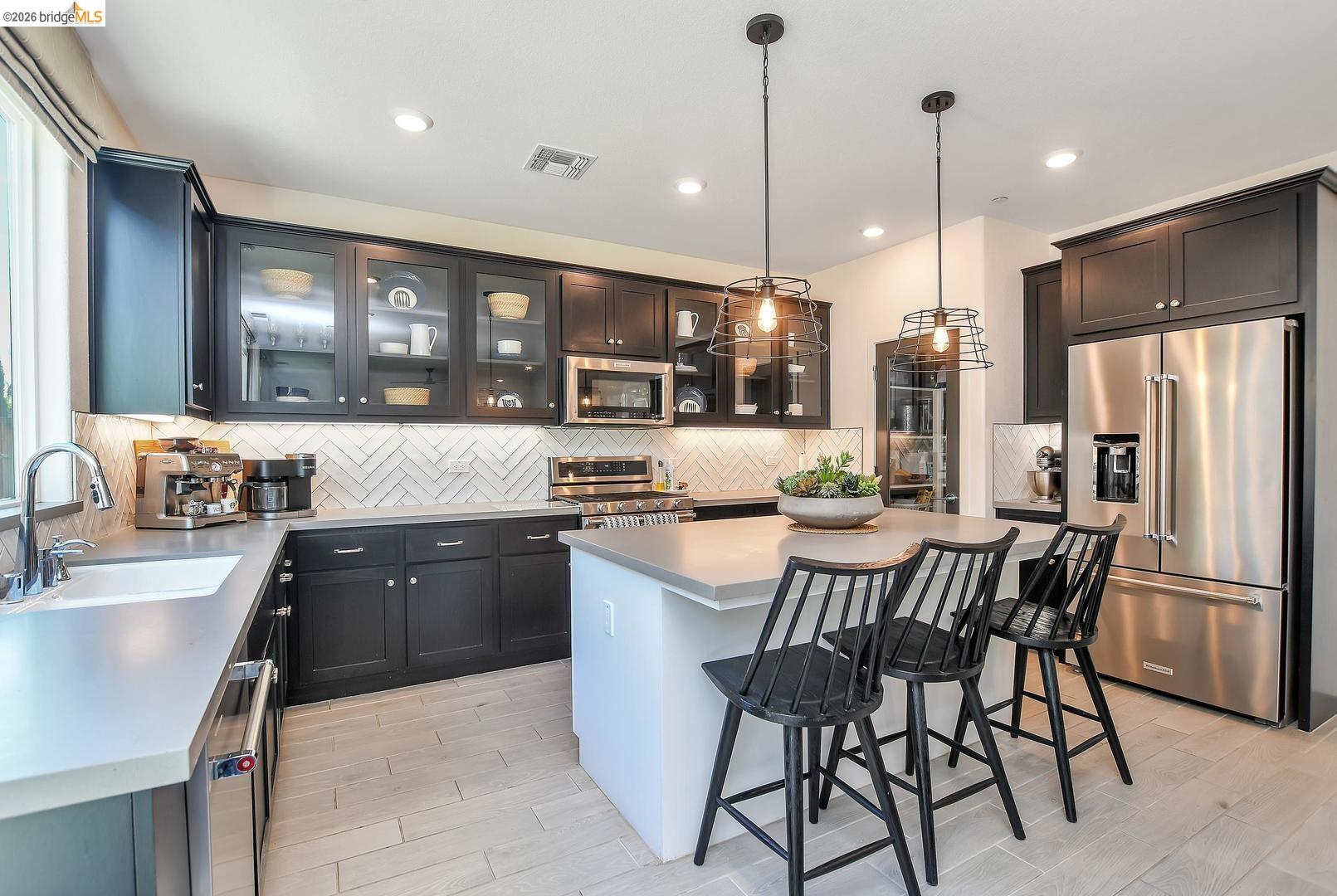 829 Hardcastle Ranch Road Oakley, CA 94561 - Photo 15 of 42 Stainless steel appliances, herringbone tile backsplash, dark wood cabinetry, light-toned countertops, and wood-finish flooring