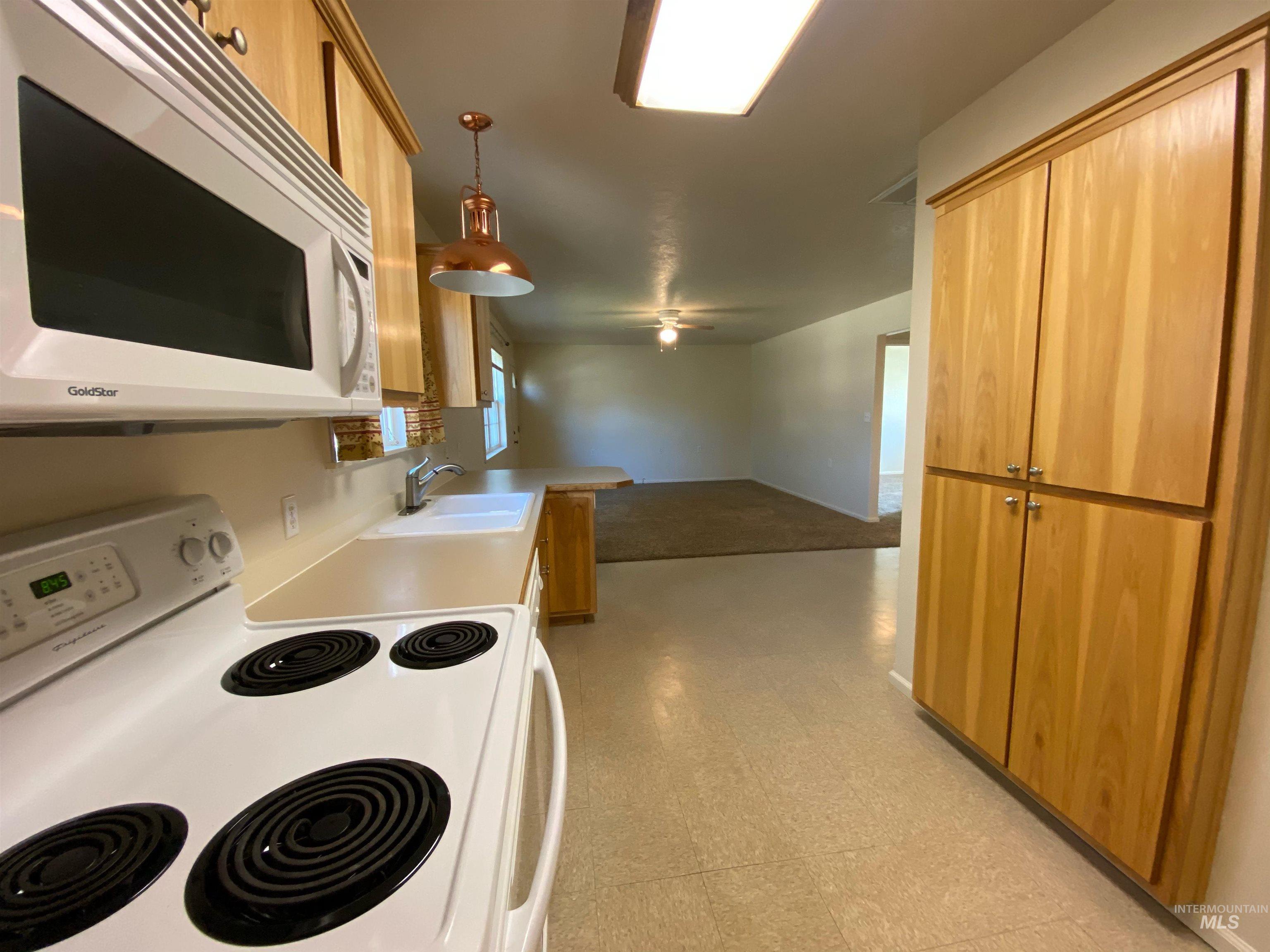 109 Adams Street Horseshoe Bend, ID 83629 - Photo 5 of 13 Kitchen with white appliances, light flooring, wood finish cabinets, hanging light fixtures, and light countertops