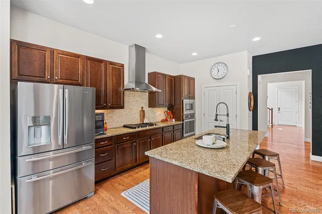 a kitchen with stainless steel appliances granite countertop a refrigerator a stove a sink and a microwave with wooden floor