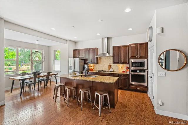 a kitchen with stainless steel appliances a stove a refrigerator a kitchen island a dining table and chairs