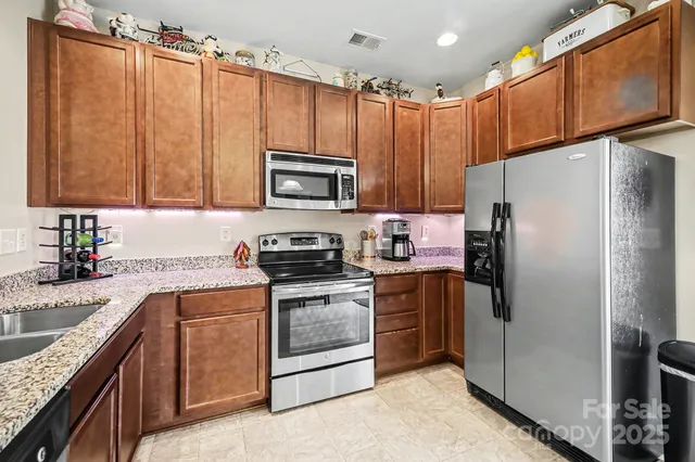 a kitchen with granite countertop a refrigerator a sink a stove top oven and cabinetry