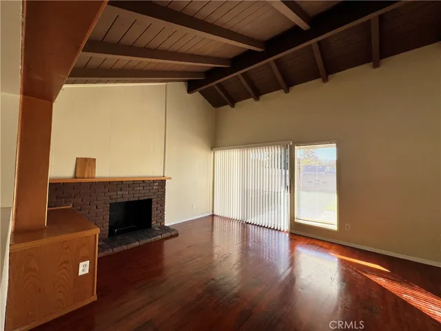 a view of an empty room with wooden floor fireplace and a window