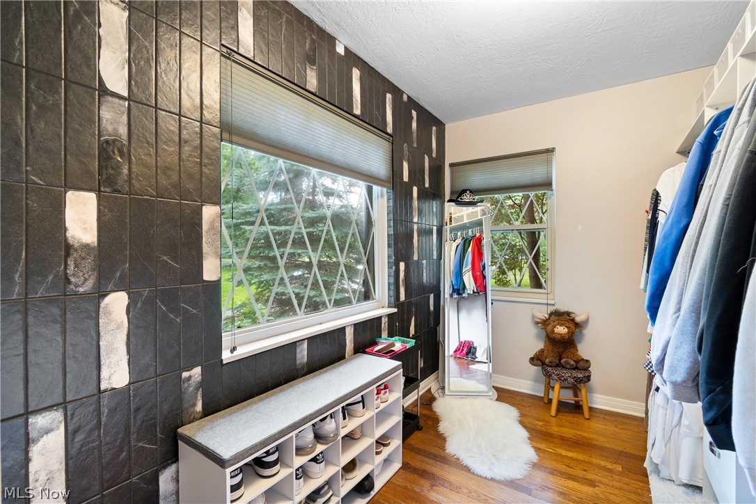 443 Merriman Road Akron, OH 44303 - Photo 29 of 44 Room featuring a distinctive dark textured accent wall with white and gray vertical tile accents, wood-finish flooring, two windows with patterned security bars, and built-in closet shelving