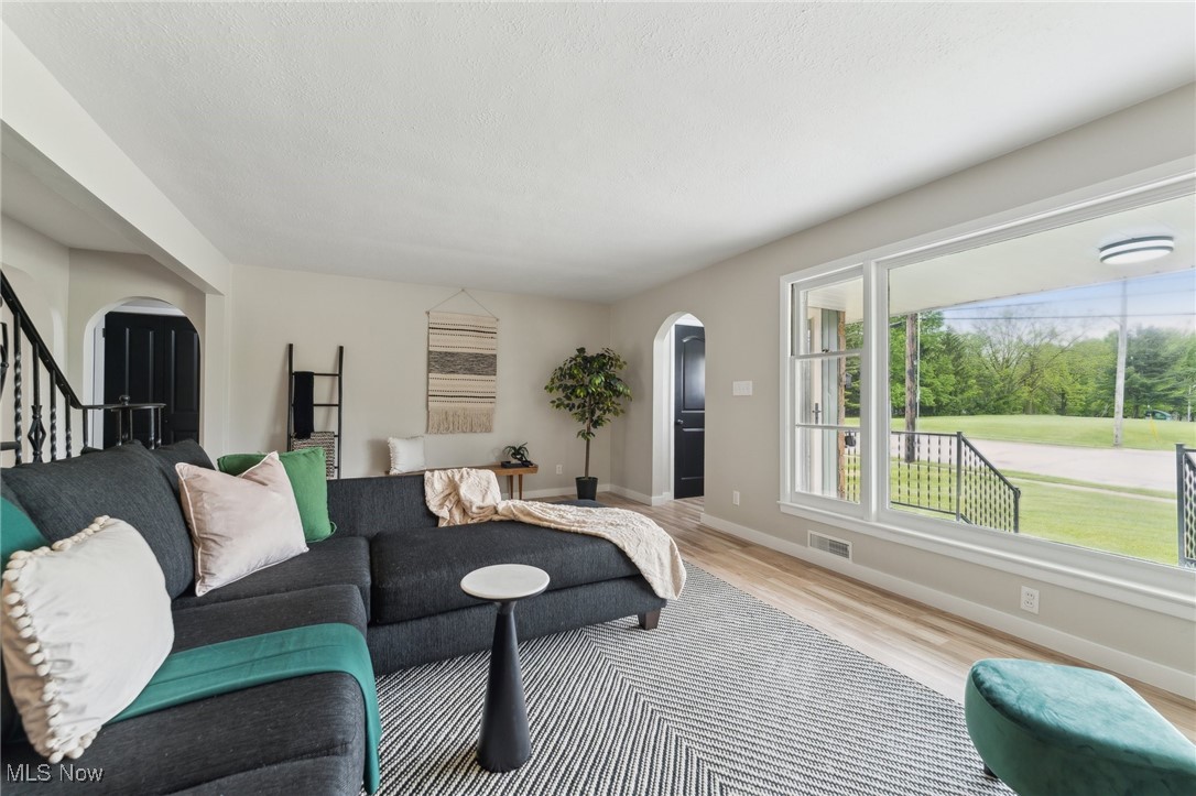 Living area featuring arched walkways, light wood-type flooring, baseboards, and stairs