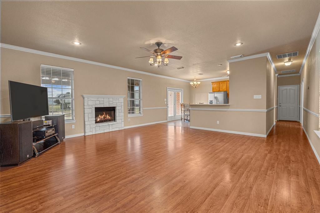 6501 Indian Trail Sanger, TX 76266 - Photo 2 of 39 Unfurnished living room with ceiling fan, light wood-style flooring, crown molding, a stone fireplace, and a chandelier