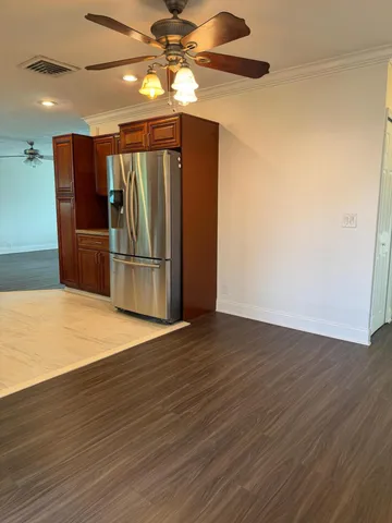 a view of a refrigerator in kitchen and an empty room with wooden floor