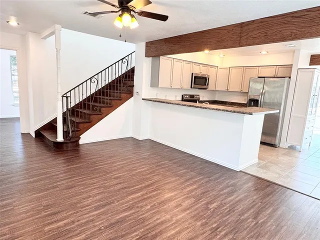 a living room with stainless steel appliances kitchen island granite countertop wooden floor a refrigerator and white cabinets