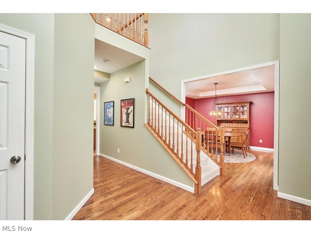 5172 Shillings Way Akron, OH 44321 - Photo 12 of 26 Staircase featuring hardwood / wood-style floors, a towering ceiling, a tray ceiling, and an inviting chandelier