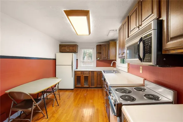 a kitchen with stainless steel appliances a stove a refrigerator a sink a dining table and chairs with wooden floor