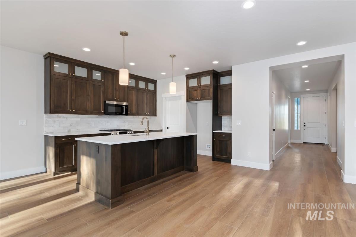 3321 Helios Street Caldwell, ID 83607 - Photo 11 of 35 Open-concept kitchen featuring wood-finish flooring, dark wood cabinetry with glass accents, light stone countertops, and a white tile backsplash