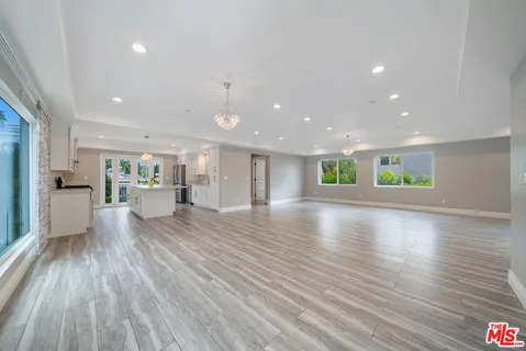 a view of an empty room and kitchen with wooden floor