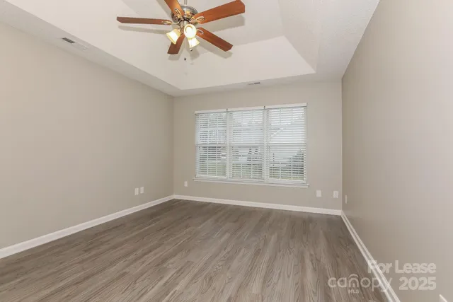 an empty room with wooden floor fan and windows