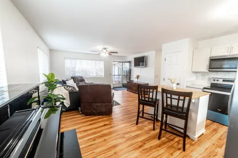 a living room with furniture a dining table wooden floor and a kitchen view