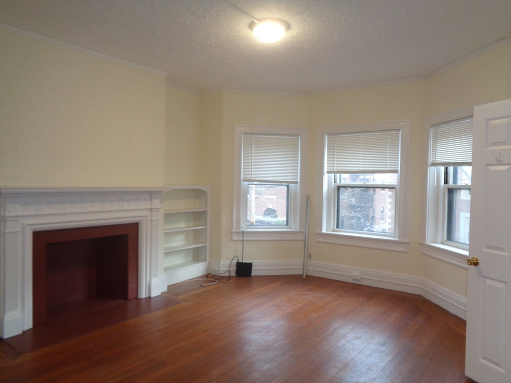 an empty room with wooden floor fireplace and windows