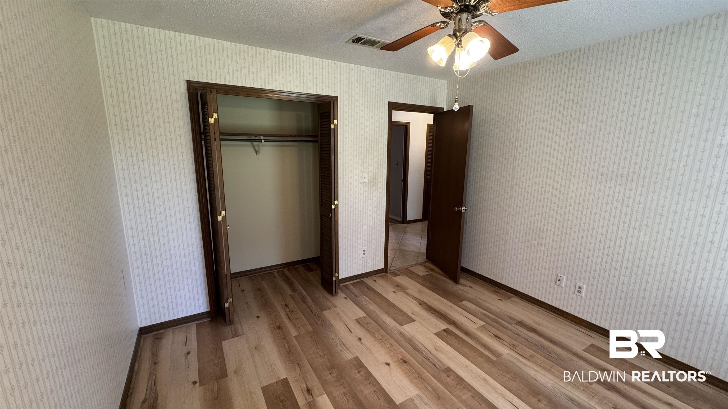 33370 Highway 98 Lillian, AL 36549 - Photo 36 of 58 Interior room featuring wood-finish flooring, patterned wallpaper, a ceiling fan with integrated lighting, and a closet with bifold doors