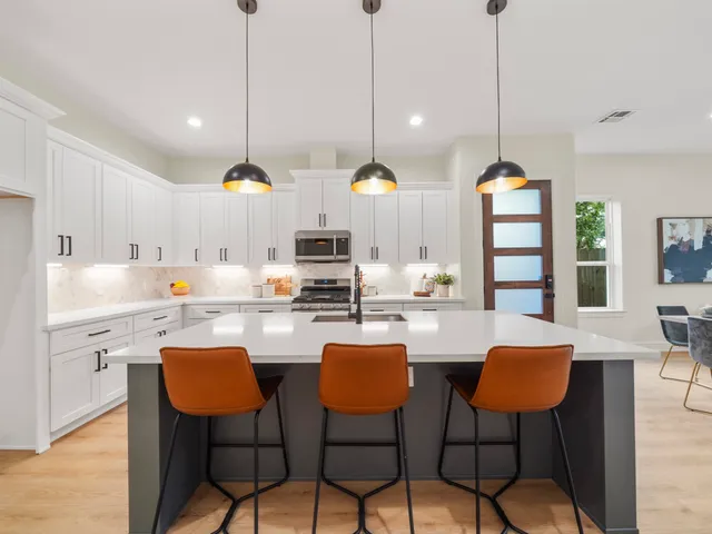 a kitchen with stainless steel appliances kitchen island a large white table chairs and white cabinets