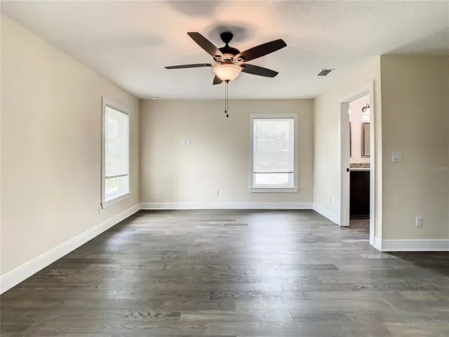 an empty room with wooden floor ceiling fan and windows