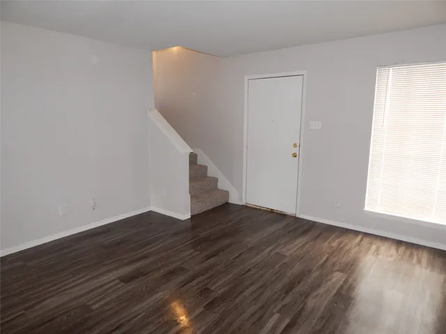 a view of an empty room with wooden floor and stairs