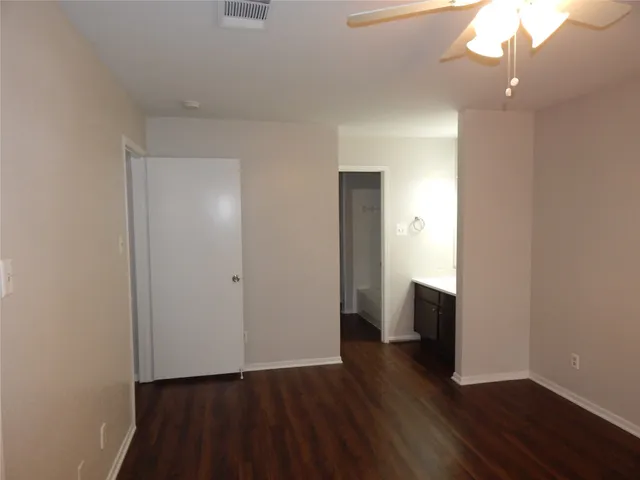 a view of an empty room with wooden floor and a ceiling fan
