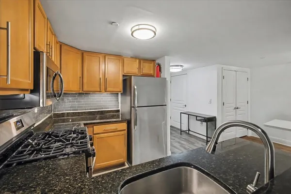a kitchen with stainless steel appliances granite countertop a refrigerator a sink a stove and white cabinets with wooden floor