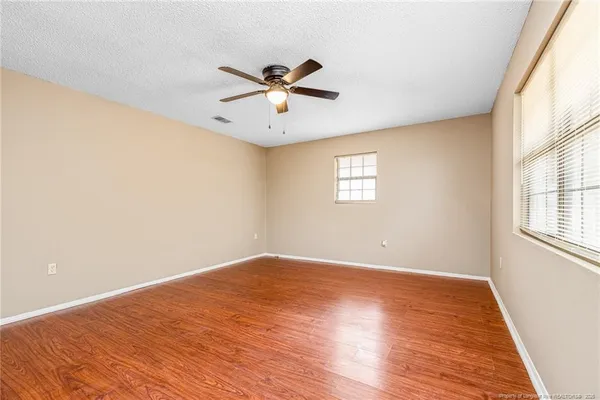an empty room with wooden floor ceiling fan and windows