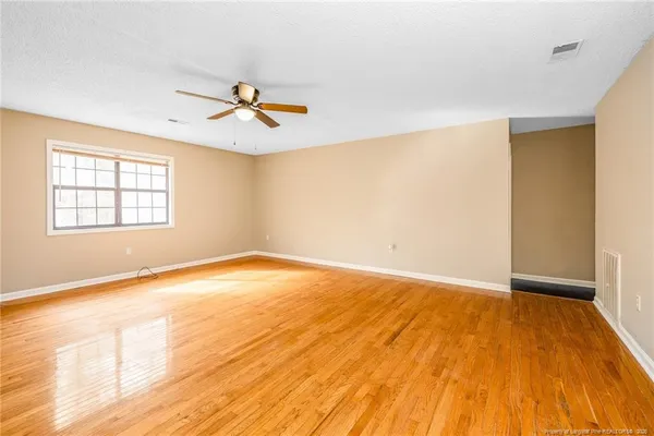 an empty room with wooden floor ceiling fan and windows