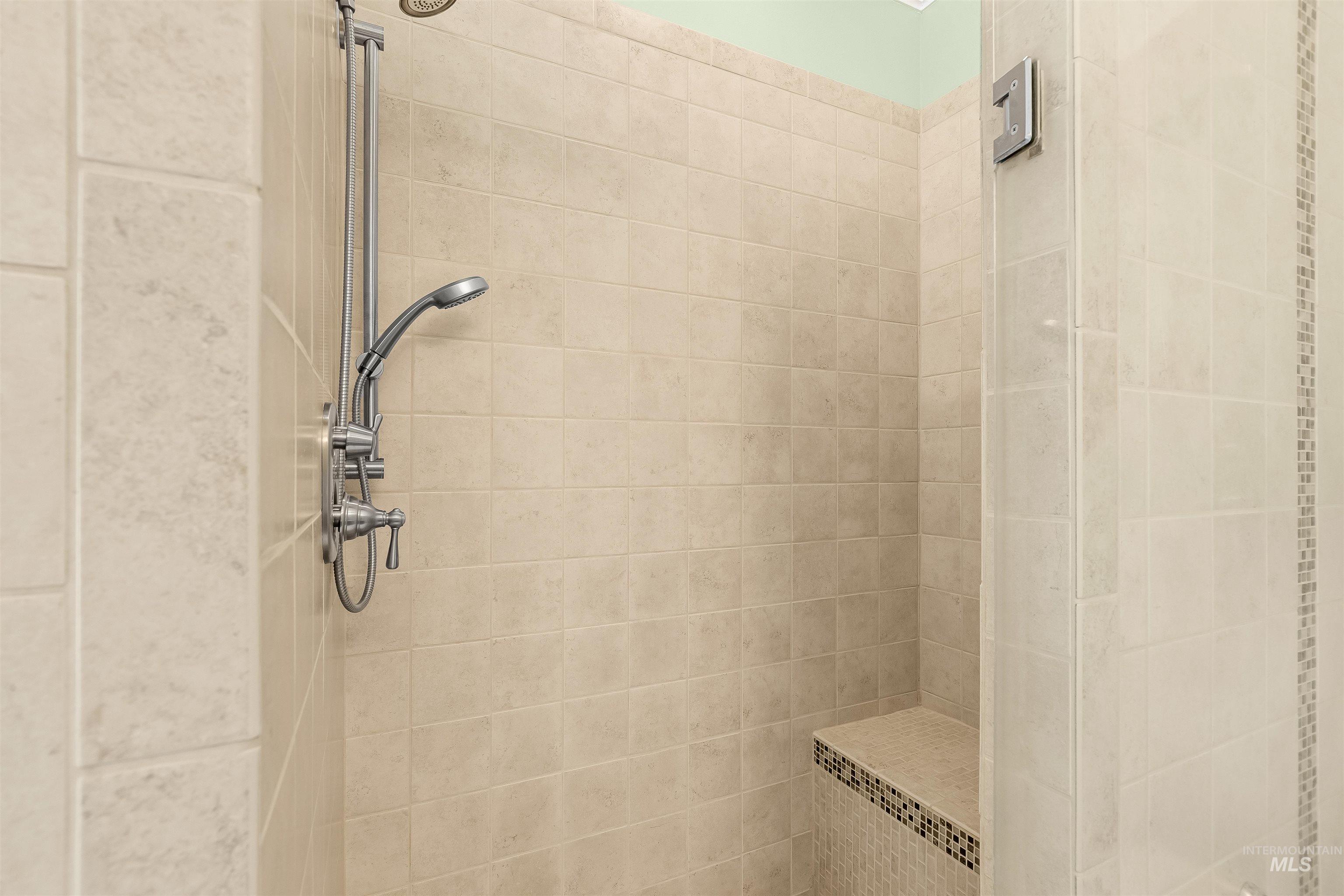 1617 Pine Cone Road Moscow, ID 83843 - Photo 23 of 44 Walk-in shower with light-toned rectangular tile surround, built-in bench featuring mosaic accent tile, and a brushed nickel shower system with handheld spray