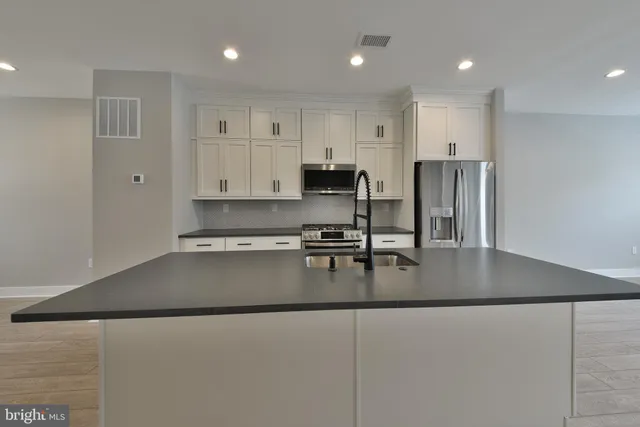 a kitchen with stainless steel appliances granite countertop a refrigerator a stove top oven a sink and a island with wooden floor