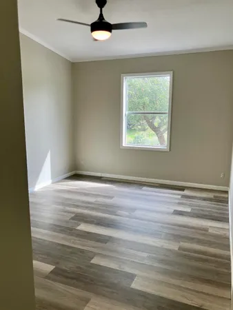 an empty room with wooden floor chandelier fan and windows