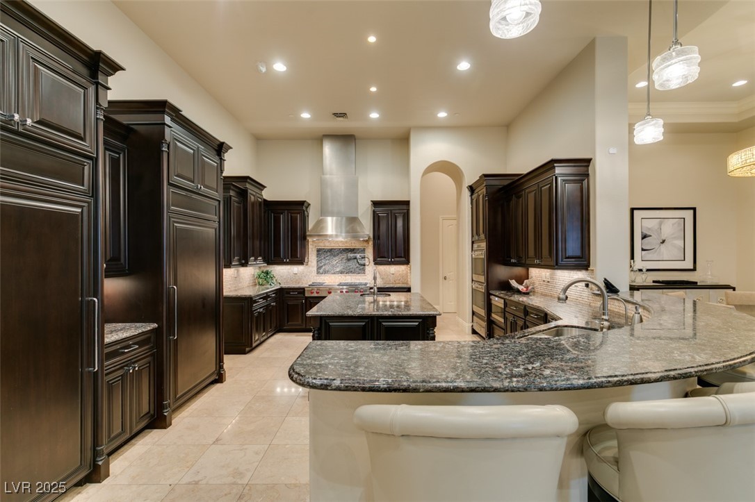 4 Awbrey Court Henderson, NV 89052 - Photo 18 of 72 Kitchen featuring dark stone countertops, hanging light fixtures, tasteful backsplash, an island with sink, and paneled built in refrigerator