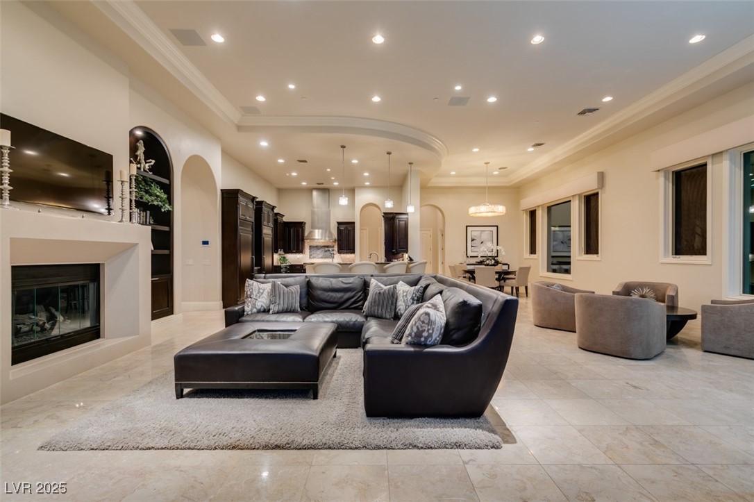 4 Awbrey Court Henderson, NV 89052 - Photo 25 of 72 Living area with arched walkways, a glass covered fireplace, recessed lighting, a tray ceiling, and built in shelves