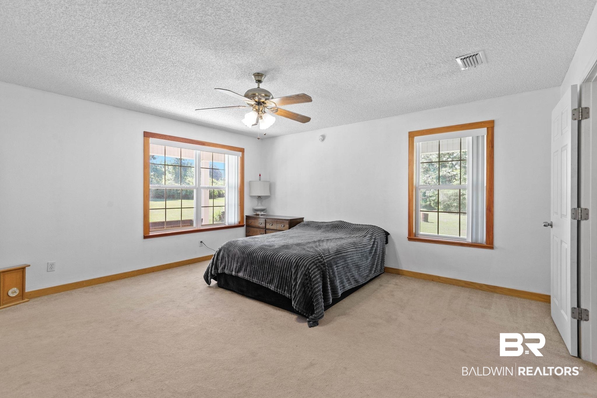 20219 Greek Cemetery Road Robertsdale, AL 36567 - Photo 22 of 41 Bright bedroom featuring two large windows with wood trim, neutral carpet, and a ceiling fan with integrated lighting