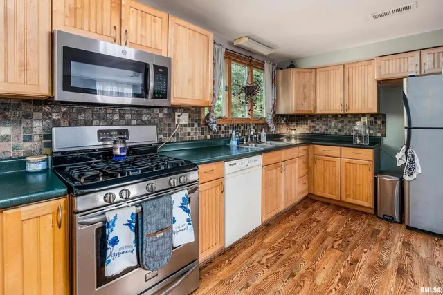 a kitchen with stainless steel appliances granite countertop a refrigerator a sink dishwasher a stove top oven a dining table and chairs with wooden floor