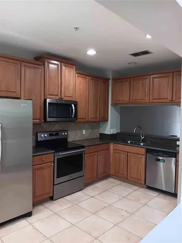 a kitchen with stainless steel appliances granite countertop a stove top oven a sink dishwasher and a refrigerator with wooden cabinets
