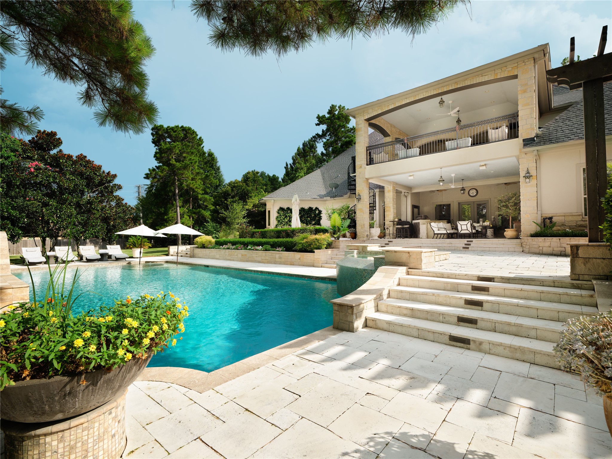 6702 Star Ledge Court Spring, TX 77389 - Photo 22 of 39 PRIVATE Grounds – Beautifully designed for both grand entertaining and peaceful everyday living, the meticulously curated outdoor living environment unfolds across expansive limestone terraces surrounding a custom pool with elegant water features. Covered gathering spaces on both levels, lush landscaping, and multiple areas for lounging and dining create a seamless connection between the home and its surroundings. Gracefully composed to balance beauty, privacy, and functionality.