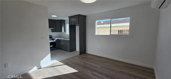 an empty room with wooden floor kitchen view and a window