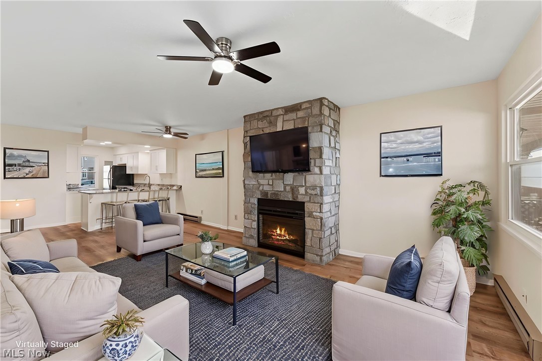 13011 West Lake Road Vermilion, OH 44089 - Photo 15 of 29 Living area featuring a stone-clad fireplace with an integrated television niche, wood-finish flooring, and a ceiling fan