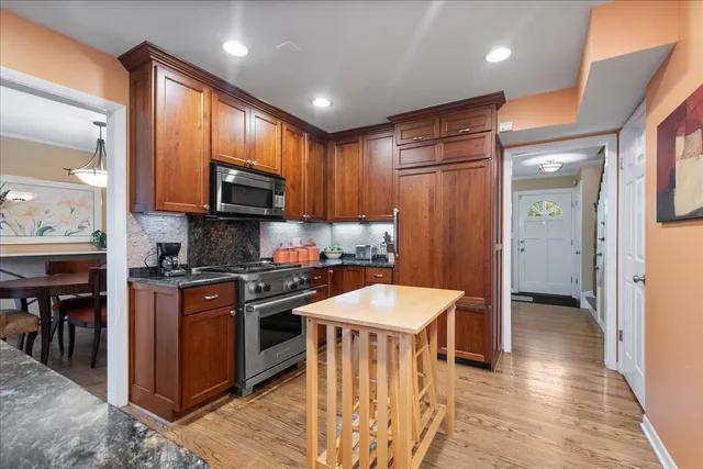 a kitchen with stainless steel appliances granite countertop a stove top oven a sink dishwasher and a refrigerator with wooden floor