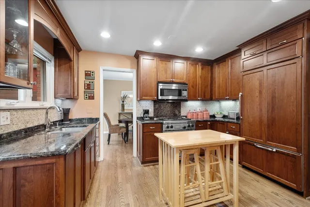 a kitchen with stainless steel appliances granite countertop a stove top oven a sink dishwasher a dining table and chairs with wooden floor