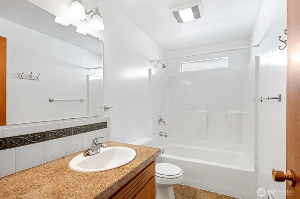 a bathroom with a granite countertop sink a toilet a mirror and shower