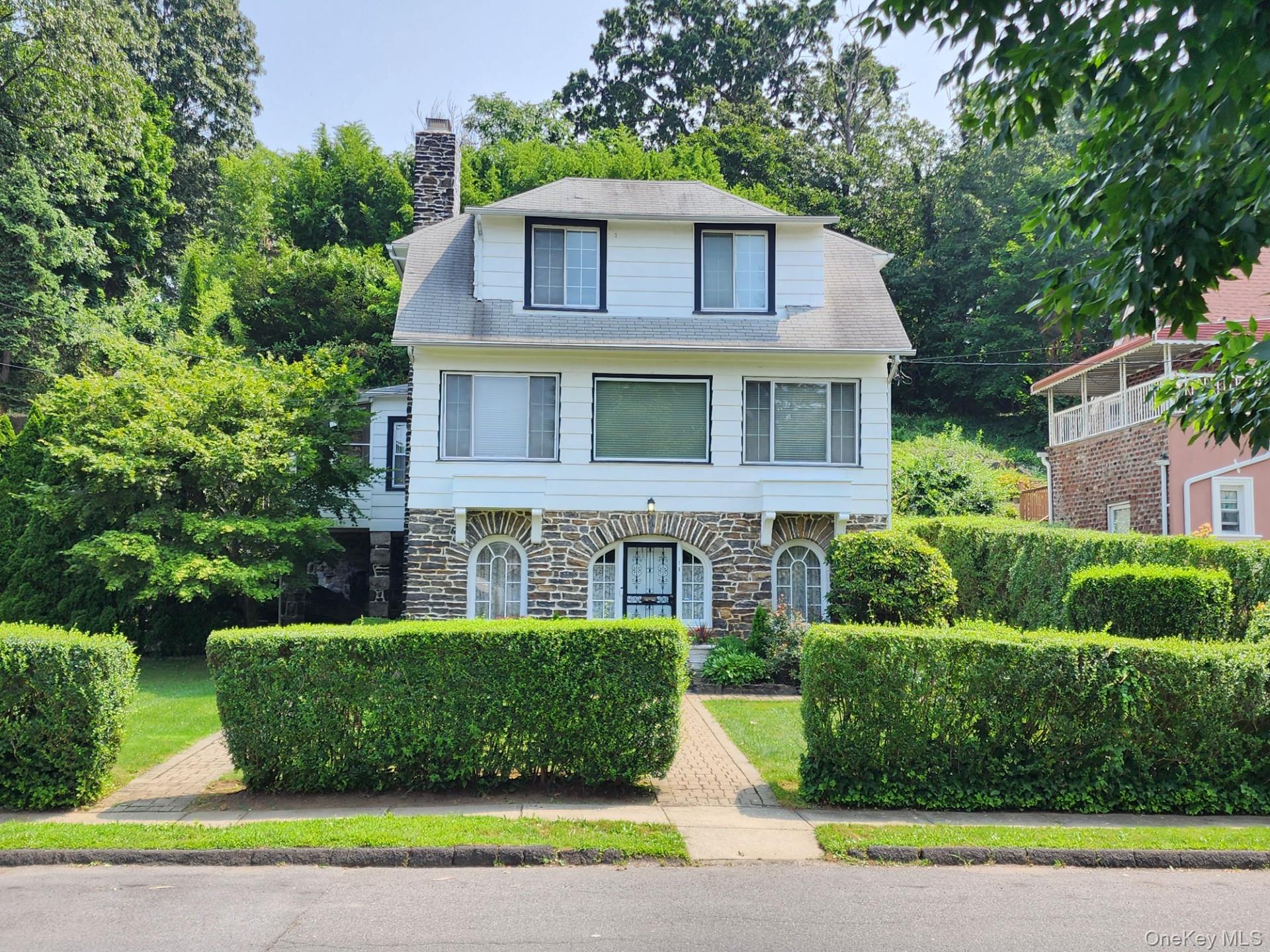 a view of a brick house with a yard plants and large trees