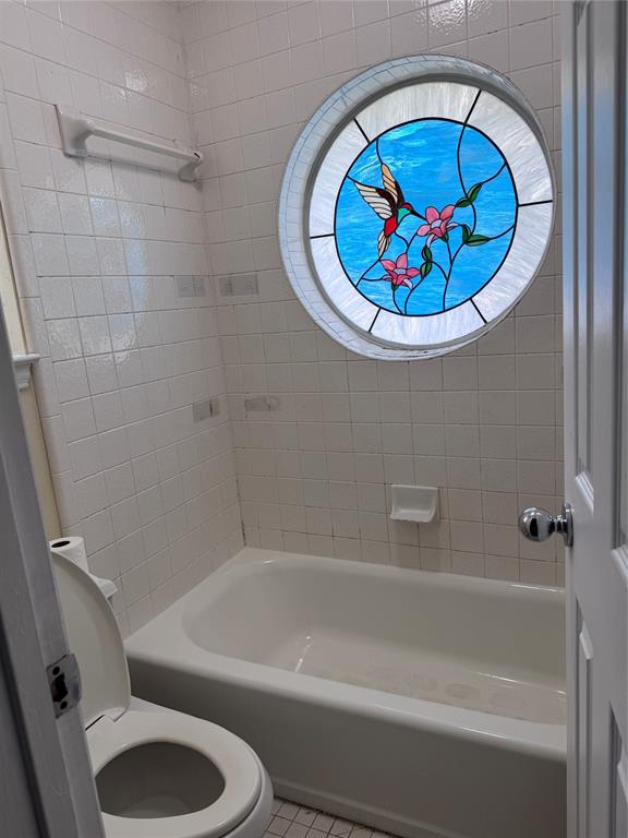 1704 South Bowen Road Pantego, TX 76013 - Photo 27 of 37 Bathroom featuring a round stained-glass window with a hummingbird motif, white ceramic wall tiling, a white built-in bathtub, and a white toilet