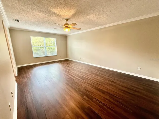 an empty room with wooden floor chandelier fan and windows