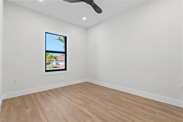 a view of an empty room with wooden floor and a ceiling fan