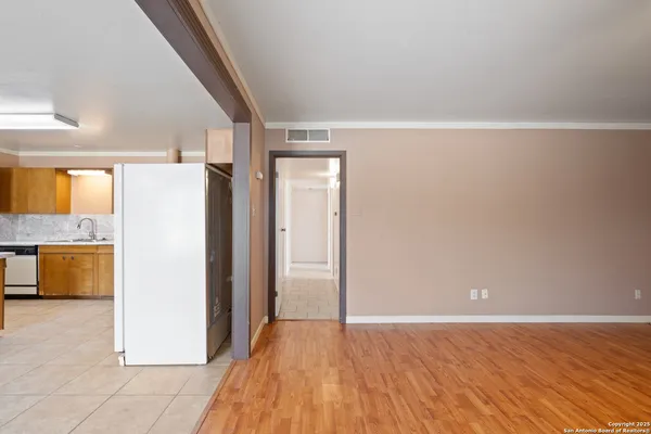 a view of a refrigerator in kitchen and an empty room with wooden floor